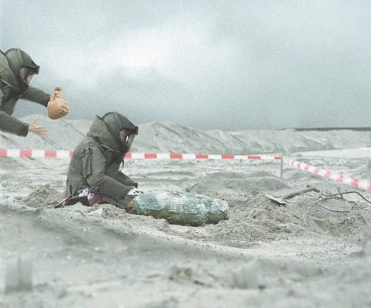 Two bomb squad workers, one is oblivious to the fact the other has blown up a paper bag and is about to pop it behind their back.